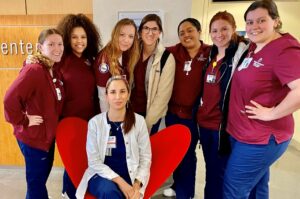 Arin Alkanani sits while surrounded by a group of student nurses in maroon scrubs.