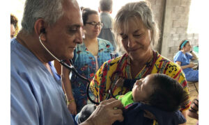Doctor and nurse use stethoscope on small child in at an outdoor clinic.