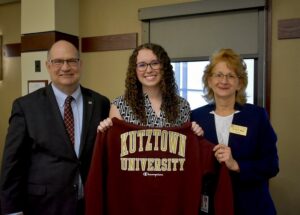 Three people stand and pose for a photo. A man stands on the left, a young woman stands in the middle holding a maroon Kutztown University sweatshirt, and a woman stands on the right. 