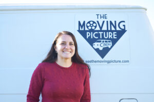 Lauren McChesney stands in front of a white van with the logo for The Moving Picture.