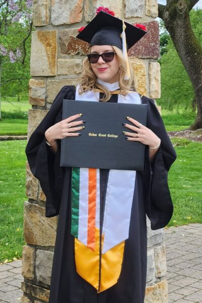 Image shows Leah Moll in graduation regalia holding her Cedar Crest College diploma.
