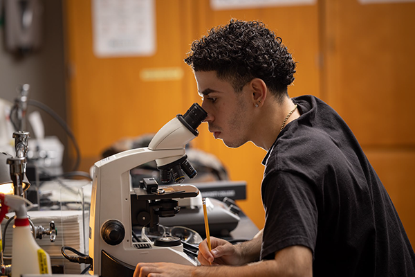 Male student in lab using microscope