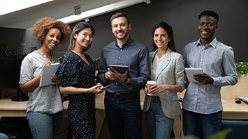 Group portrait of smiling multiethnic millennial work team standing together looking at camera in office, happy young multiracial diverse colleagues posing for picture show unity and partnership